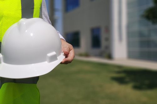 close up of a person in a yellow vest holding a hard hat