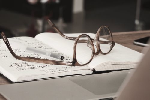 glasses on top of a notebook in front of a laptop