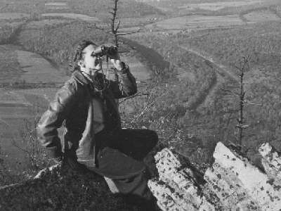 Rachel Carson, sitting on a peak, watching migrating hawks through binoculars at Hawk Mountain, PA., in 1945.