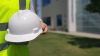 close up of a person in a yellow vest holding a hard hat